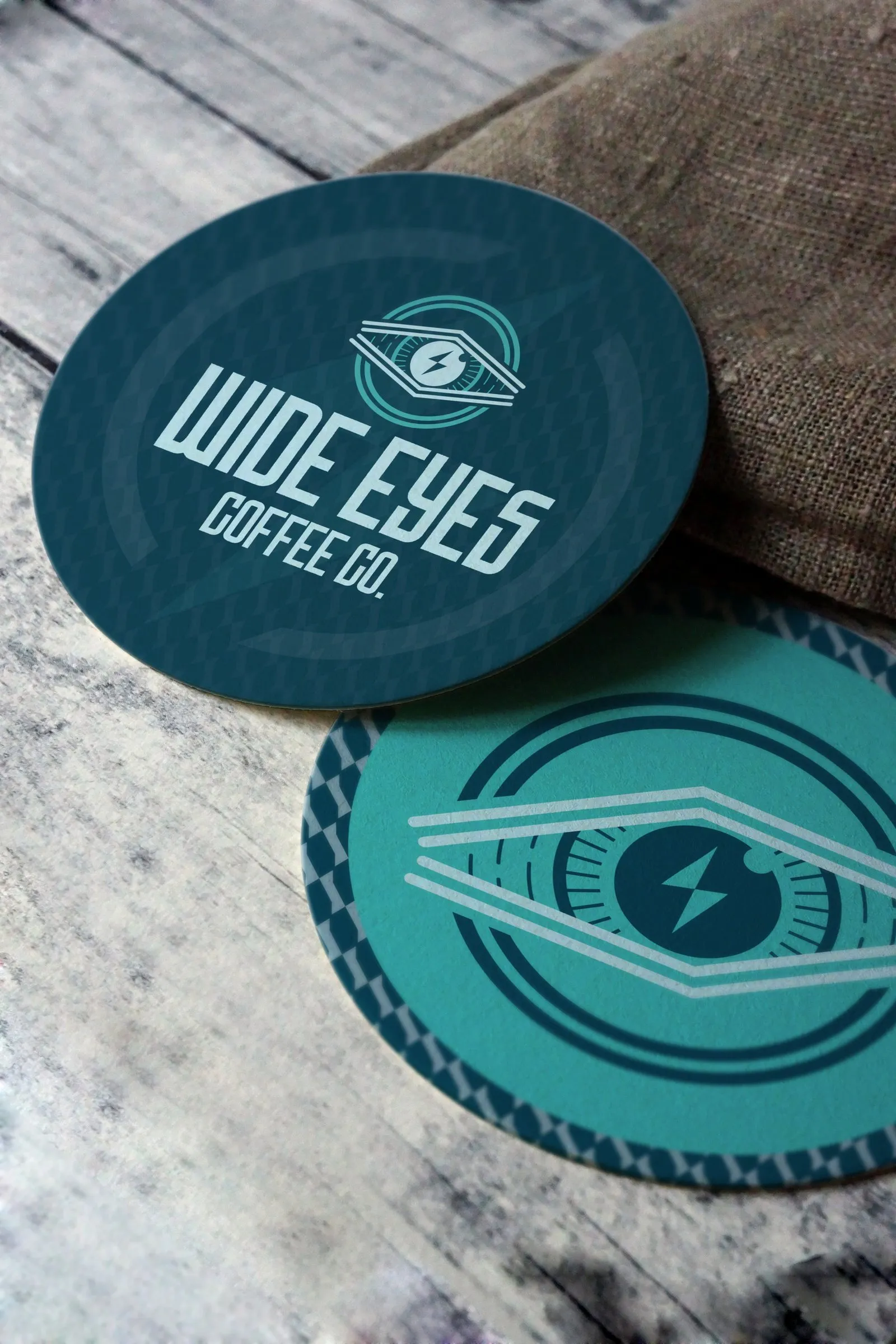 Wide Eyes coasters on a wooden table, wordmark side and mark side