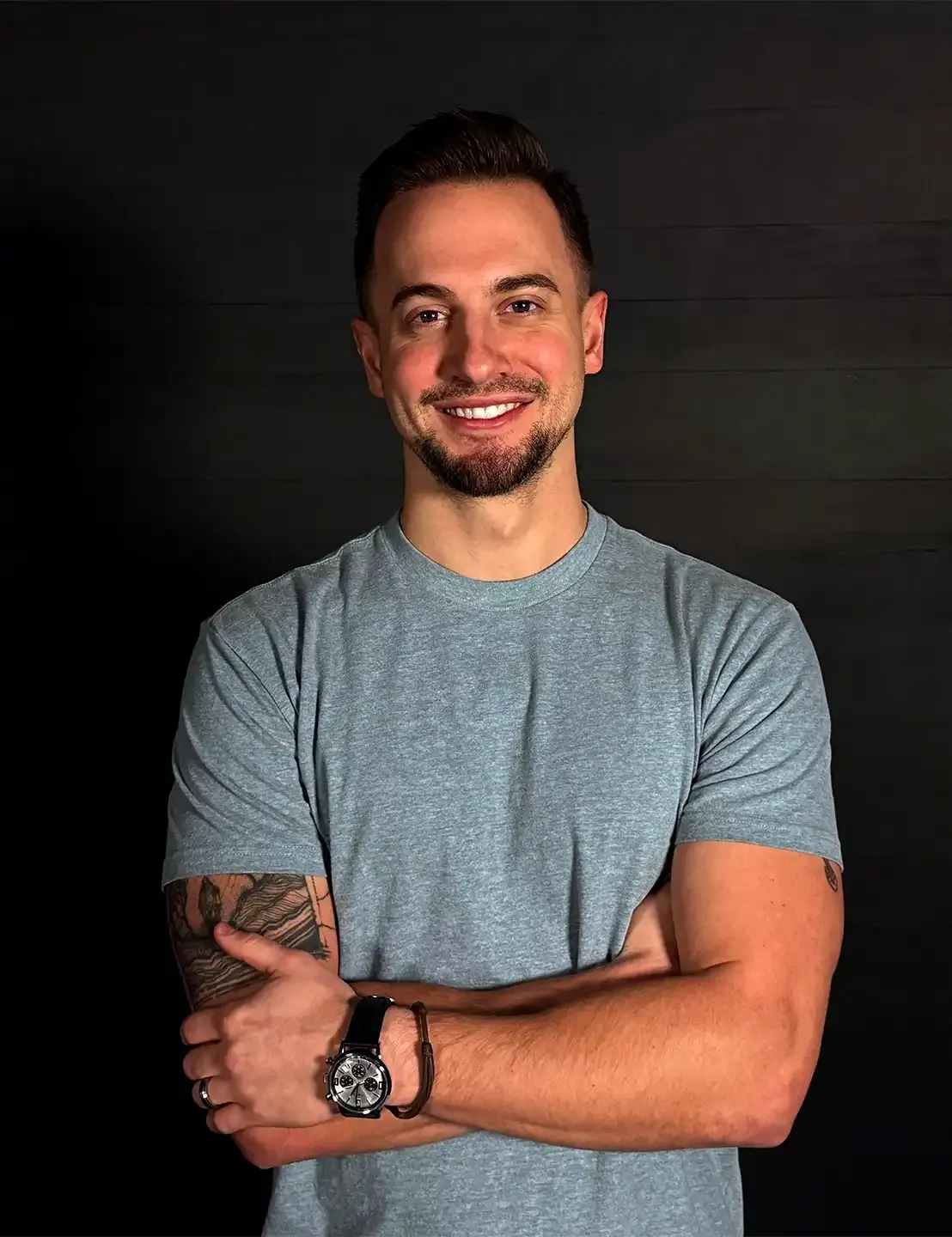 Danny Sobek, arms crossed, smiling, against a dark wood wall