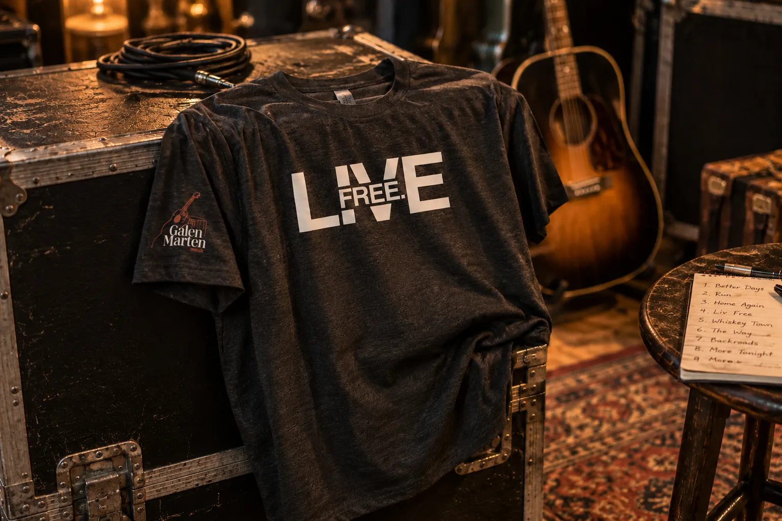 The Live Free tee on a road case beside a guitar and a set list
