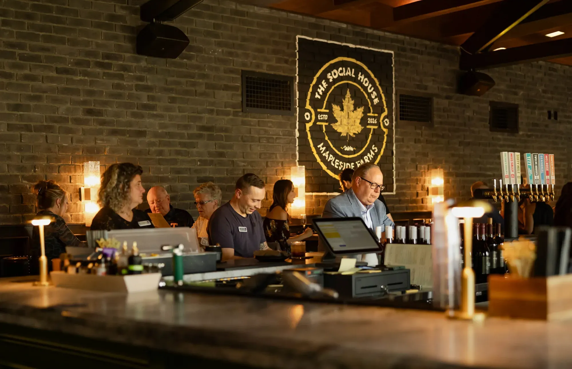 The Social House bar in service, the badge on the brick wall above the staff and the taps