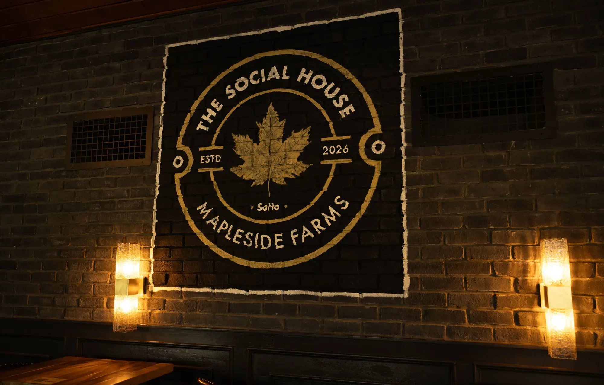 The Social House badge painted in cream on the grey brick wall behind the bar, between two sconces